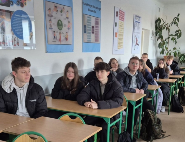 Zdjęcie przedstawia uczniów siedzących w ławkach w klasie, na ścianach plakaty tematyczne.