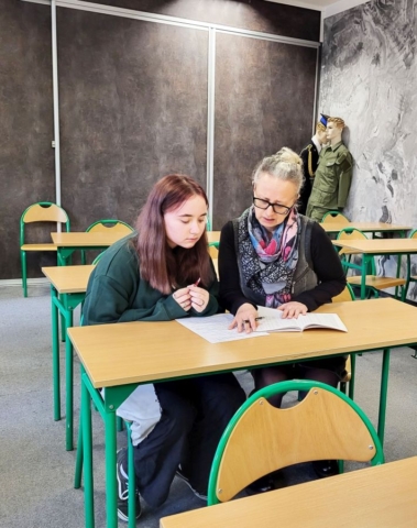 Obrazek przedstawia dwie osoby, panią doradcę zawodowego i ucznia, siedzących przy ławce. Na ławce znajdują się dokumenty. Zdjęcie ilustruje wpis o praktyce zawodowej i dotyczy zajęć z doradztwa zawodowego.