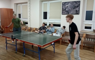 dzien_kobiet_internat5 Zdjęcie zrobione w świetlicy internatu przedstawia dwóch uczniów grających w tenisa stołowego. W tle 3 osoby kibicujące kolegom.