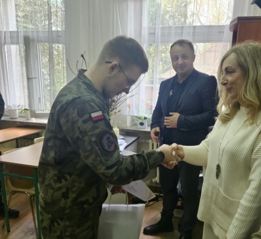Zdjęcie przedstawia ucznia, zwycięzcę konkursu historycznego, odbierającego nagrodę rzeczową i dyplom z rąk organizatorów konkursu.