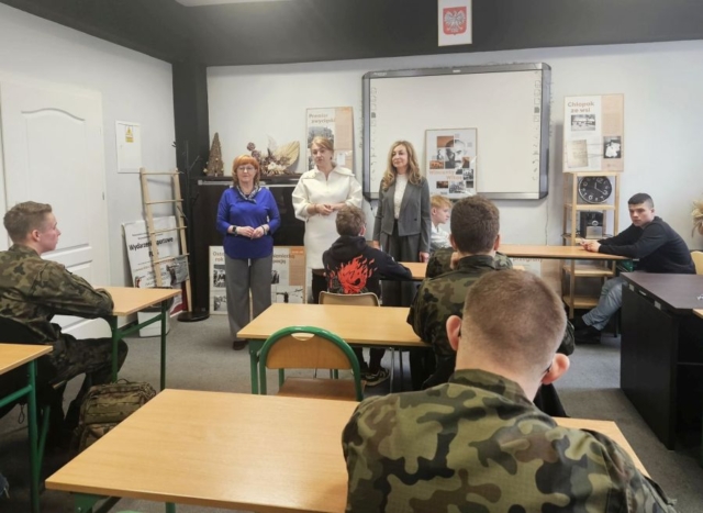 konkurs_historyczny1 Wnętrze sali konferencyjnej, uczniowie (kilku w mundurach klasy mundurowej) siedzą w ławkach. Przed nimi stoją 3 kobiery i przemawiają. W tle tablica multimedialna, godło Polski, zegar. Widać też tablicę ze zdjęciami z wizerunkiem Wincentego Witosa.