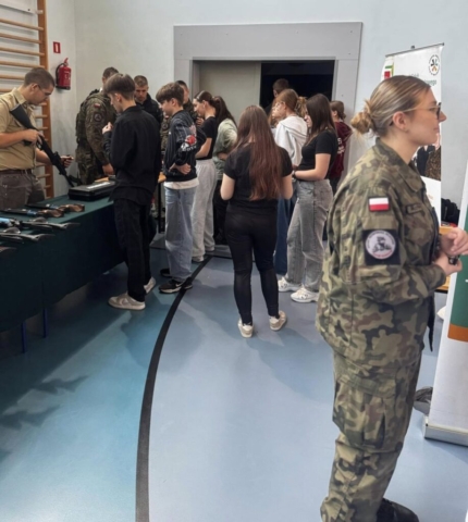 Zdjęcie przedstawia uczniów biorących udział w targach edukacyjnych. Po prawej stronie rollupy szkoły, po lewej stoisko.