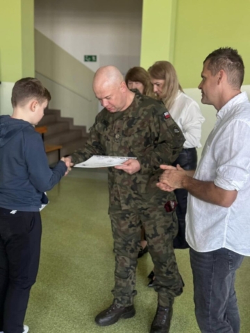 Zdjęcie przedstawia 5 osób. 4 dorosłych i jeden chłopiec. Jeden z dorosłych wręcza chłopcu dyplom.