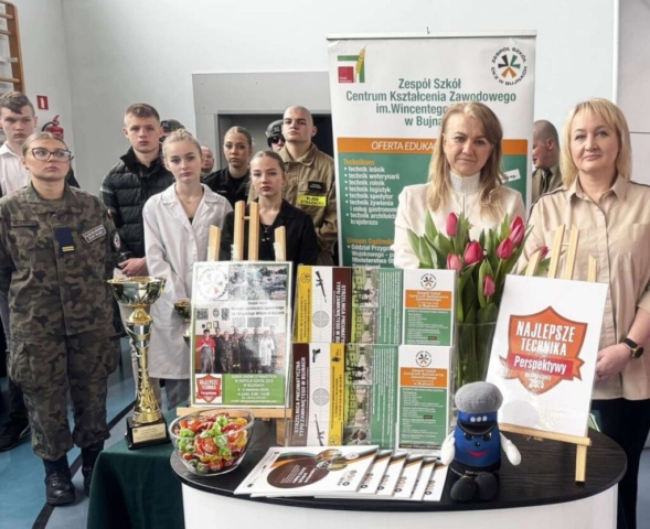 Zdjęci przestawia uczniów, p. Dyrektor oraz p. Pedagog reprezentujących szkołę na targach edukacyjnych oraz stoisko szkoły. W tle rollup Zespołu Szkół Centrum Kształcenia Zawodowego im. Wincentego Witosa w Bujnach.