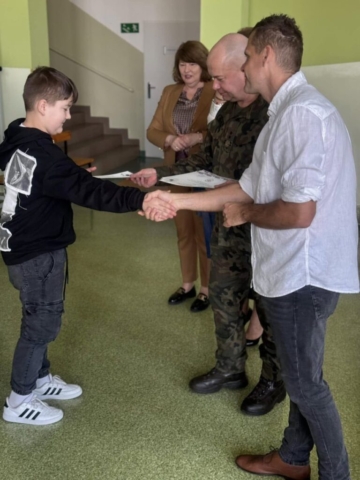 Zdjęcie przedstawia ucznia otrzymującego dyplom i gratulacje.