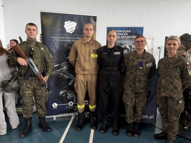 Zdjęcie przedstawia uczniów reprezentujących szkołę oraz panią żołnierz na tle baneru WCR Tomaszów Mazowiecki.