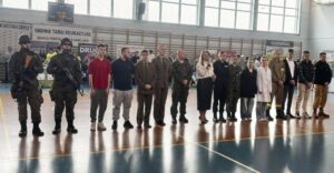 Zdjęcie przedstawia uczniów, Panią Dyrektor oraz opiekuna młodzieży, stojących w rzędzie na sali gimnastycznej. W tle drabinki gimnastyczne i baner z napisem Gminne Targi Edukacyjne. 