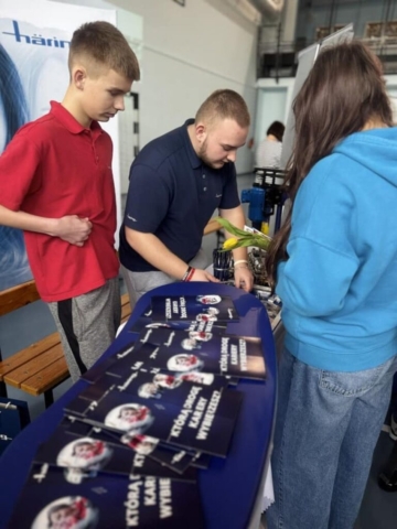 Zdjęcie przedstawia uczniów reprezentujących szkołę podczas targów edukacyjnych oraz stoisko partnera szkoły Haering.