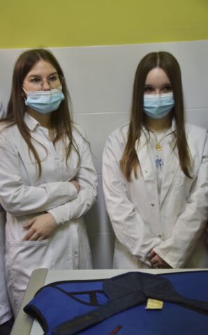 Uczestniczki praktyki zagranicznej w fartuchach i maseczkach w pomieszczeniu. Widoczny także stół laboratoryjny a na nim ochraniacz używany do zdjeć RTG.