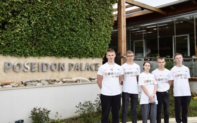 5 uczestników wyjazdu w koszulkach firmowych przed wejściem do hotelu - Poseidon Palace.