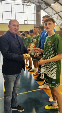 Drużyna sportowa w hali sportowej odbiera trofeum z rąk organizatora zawodów.