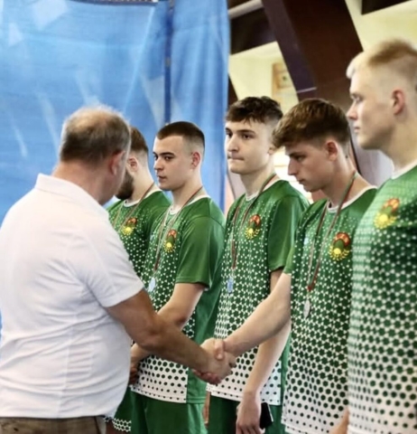 5 zawodników w strojach sportowych koloru zielonego i białego z logo LZS na koszulkach. Odbierają medale i gratulacje z rąk organizatora. Zawodnicy mają na szyjach medale.