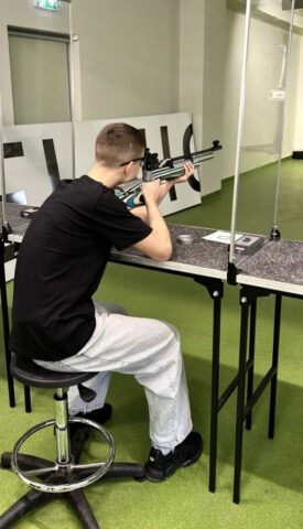 mks_piotrkowianin_strzelnica04 Zawodnik siedzi na stanowisku strzelniczym, trzyma broń i przygotowuje się do strzału.