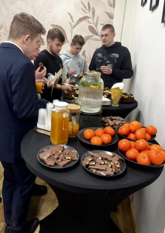 5 uczniów stoi przy stolikach z poczęstunkiem. Dwóch z nich trzyma dyplomy.