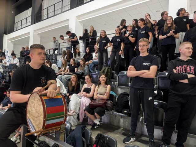 puchar_komendanta_policji01 Trybuny sportowe w hali. Kibice ze szkół biorących udział w finale pucharu. Na pierwszym planie po lewej stronie uczeń siedzi na barierce i trzyma bęben.
