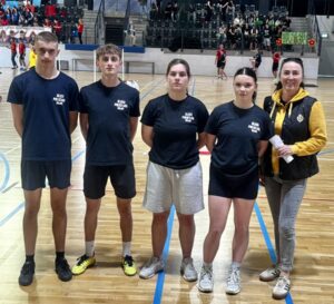 Zawodnicy biorący udział w finale konkursu o Puchar Komendanta Policji wraz z opiekunem wewnątrz hali sportowej. W tle trybuny, kibice i inni zawodnicy.