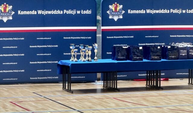 puchar_komendanta_policji07 Ławki przykryte granatowym suknem, na których stoją torby reklamowe oraz puchary. W tle banery reklamowe Komendy Wojewódzkiej Policji w Łodzi.