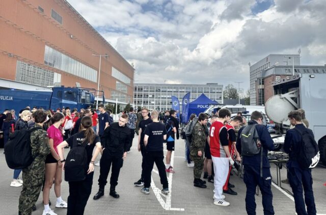 puchar_komendanta_policji08 Uczniowie na zewnątrz. W tle zabudowania oraz namioty reklamowe Policji, a także samochody policyjne.