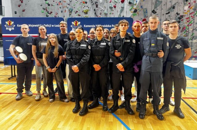 puchar_komendanta_policji09 Uczniowie w umundurowaniu wraz z opiekunem, kibice i zawodnicy finału turnieju o Puchar Komendanta Policji w hali sportowej na tle banerów reklamowych Komendy Wojewódzkiej Policji w Łodzi.