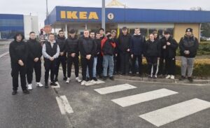 Grupa młodzieży stoi na zewnątrz, w tle budynek z logo firmy IKEA.  