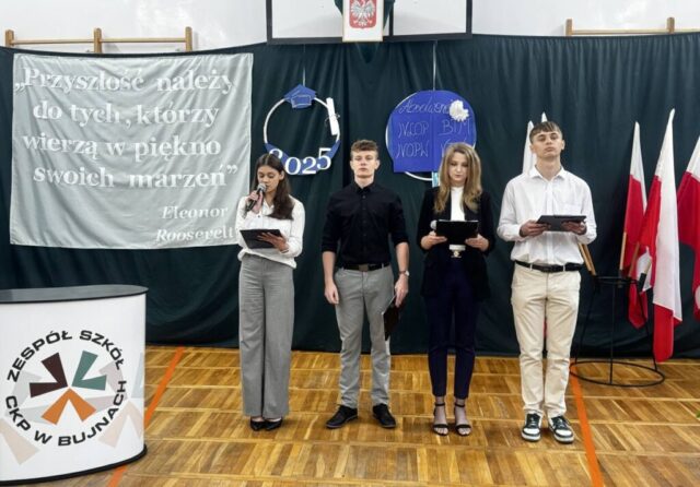 2 uczennice i 2 uczniów prowadzących uroczystość zakończenia roku szkolnego dla maturzystów. W tle napis na szarym materiale "Przyszłość należy do tych, którzy wierzą w piękno swoich marzeń" Eleonor Roosevelt, dekoracje obręcz z biretem oraz zwiniętym dyplomem i rokiem 2025 oraz kolejny napis na granatowym tle absolwenci IV LOp, IV OPW, BTM, VTWL. Po prawej stronie stojak z flagami Polski. Po lewej stół promocyjny z logo szkoły i napisem Zespół Szkół CKP w Bujnach.