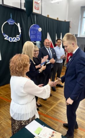 Uczeń klasy maturalnej odbiera gratulacje od p. Wicedyrektor, obok stoją także p. Dyrektor, p. Wychowawczyni oraz p. Wicestarosta i zaproszeni goście.