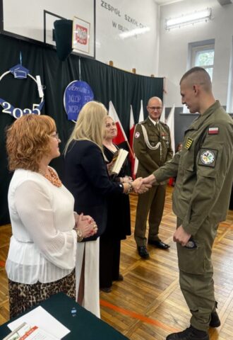 Absolwent klasy opw w umundurowaniu odbiera z rąk p. Dyrektor gratulacje i nagrodę książkową. Towarzyszą p. wicedyrektor, wychowawca i zaproszony przedstawiciel służb mundurowych.