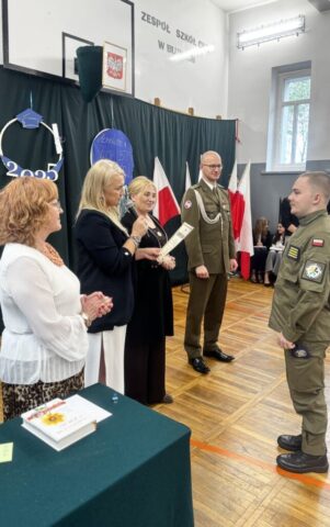 Absolwent klasy opw w umundurowaniu stoi przed zgormadzoną w sali gimnastycznej Dyrekcją, wychowawcą i przedstawicielem służb mundurowych. P. Dyrektor przemawia i za chwilę wręczy absolwentowi dyplom.