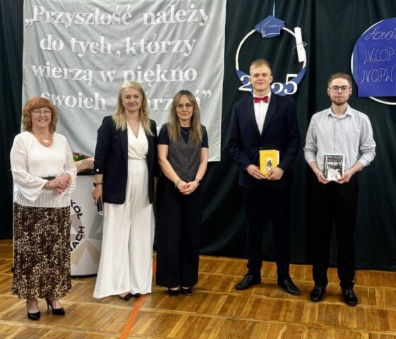 2 uczniów klas maturalnych, p. Dyrektor, p. Wicedyrektor i p. nauczycielka. Uczniowie trzymają w rękach nagrody książkowe. W tle napis przewodni uroczystości i dekoracje.