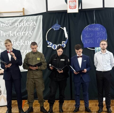 Przedstawiciele klas maturalnych przemawiają podczas uroczystości zakończenia roku szkolnego. W tle częściowo widoczny napis przewodni uroczystości oraz dekoracje.