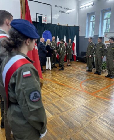 Przedstawiciele służb mundurowych, p. dyrektor, p. Wicestarosta i absolwenci klasy OPW w umundurowaniu odbierają certyfikaty. Widoczny także częściowo poczet sztandarowy szkoły.