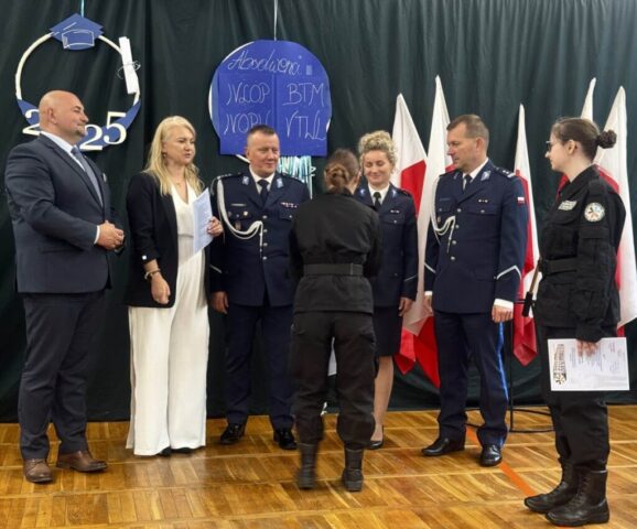 Uroczystość zakończenia roku szkolnego klas maturalnych w sali gimnastycznej. Przedstawiciele służb mundurowych policji, p. Dyrektor, p. Wicestarosta oraz dwie absolwentki klasy policyjnej. Uczennice odbierają certyfikaty.