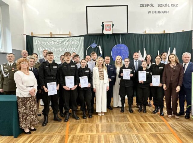 Uroczystość zakończenia roku szkolnego klas maturalnych. Absolwenci klasy policyjnej w mundurach, Dyrekcja, wychowawca, zaproszeni goście- przedstawiciele służb mundurowych i władz lokalnych w udekorowanej na okoliczność sali gimnastycznej. Absolwenci trzymają w rękach certyfikaty i dyplomy.
