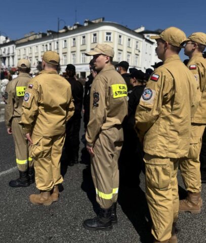 Uczniowie klas mundurowych (klasa strażacka, klasa policyjna) na obchodach rocznicy uchwalenia Konstytucji 3 Maja. W tle białe zabudowania.