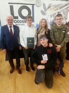 3 finalistów konkursu historycznego Żołnierze Wyklęci obudźcie Polskę wraz z opiekunem i organizatorem. W tle baner szkoły LO Poddębice. 