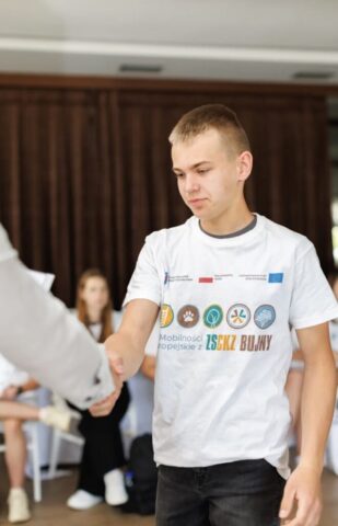 Uczestnik zagranicznych praktyk zawodowych odbiera gratulacje . W tle inni uczestnicy praktyk.