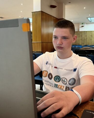 Uczestnik zagranicznej praktyki zawodowej siedzi przy komputerze. Pracuje nad czymś w skupieniu.