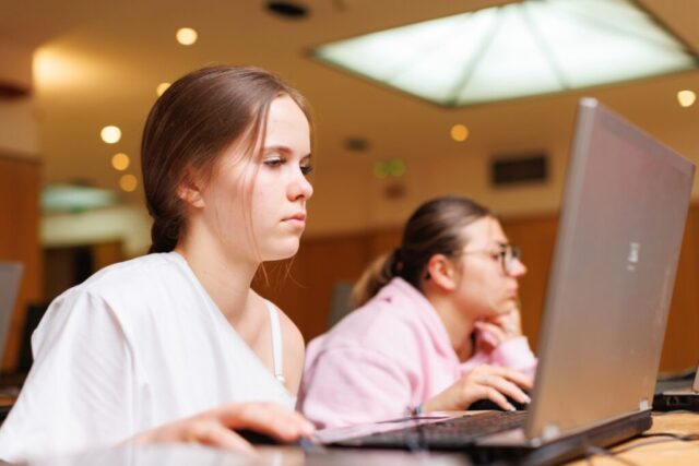 2 uczestniczki zagranicznej praktyki zawodowej siedzą w pomieszczeniu przy biurkach. Pracują nad czymś na laptopach.