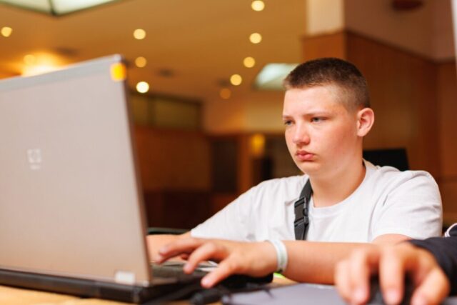 Uczestnik zagranicznej praktyki zawodowej siedzi w pomieszczeniu. Wykonuje pracę na laptopie. Skupiony patrzy w ekran.