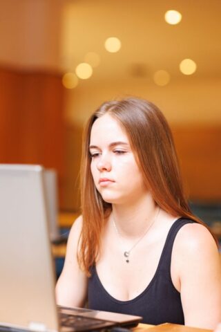Uczestniczka zagranicznej praktyki zawodowej w pomieszczeniu. Siedzi przy ławce, na której stoi laptop i patrzy w ekran.