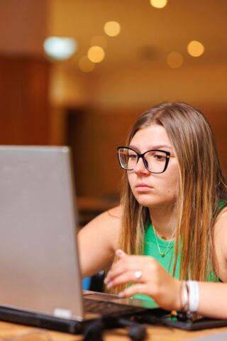 Uczestniczka zagranicznej praktyki zawodowej w pomieszczeniu. Siedzi przy ławce, na której stoi laptop i patrzy w ekran.