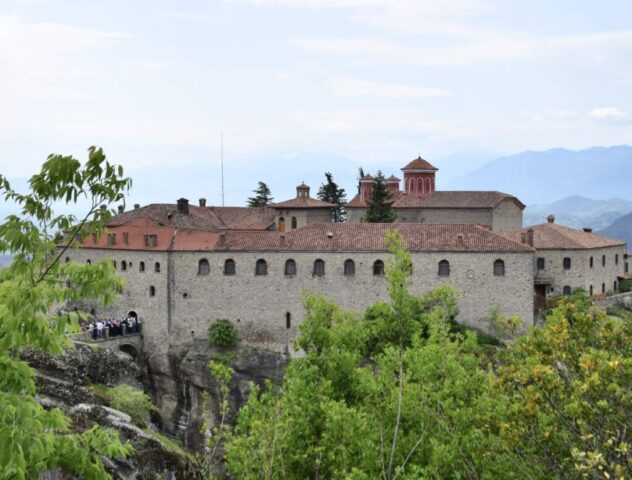 Obszerne zabudowania klasztoru w Meteorach. W tle wzgórza. Po lewej stronie w oddali turyści czekający na wejście do klasztoru.