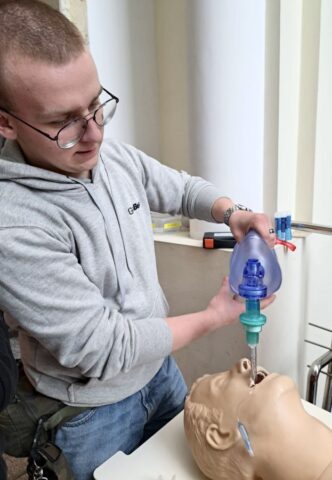 Uczestnik konkursu wewnątrz pomieszczenia. Za pomocą resuscytatora demonstruje na fantomie udzielanie pierwszej pomocy.