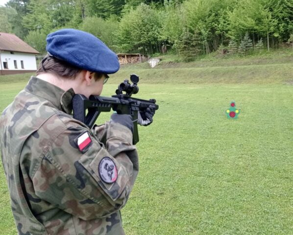 Uczestnik obozu szkoleniowego w umundurowania podczas ćwiczeń w terenie ze strzelania do celu. W tle budynek i las.