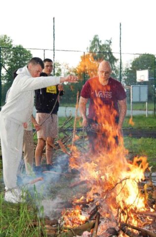 Uczniowie klas mundurowych na terenie boiska szkolnego w trakcie ogniska. Smażą kiełbaski.