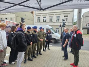 Grupa uczniów, część w umundurowaniu przed budynkiem Archiwum Państwowego w Piotrkowie Trybunalskim. Stoją i słuchają pracowników tego Archiwum. 