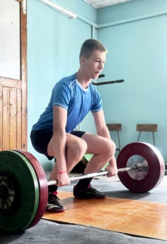 Uczestnik wieloboju sportowego w trakcie podnoszenia ciężarów wewnątrz klubu sportowego.