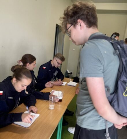 Uczniowie klasy mundurowej przy ławkach dokonują rejestracji uczestników zmagań sportowych.