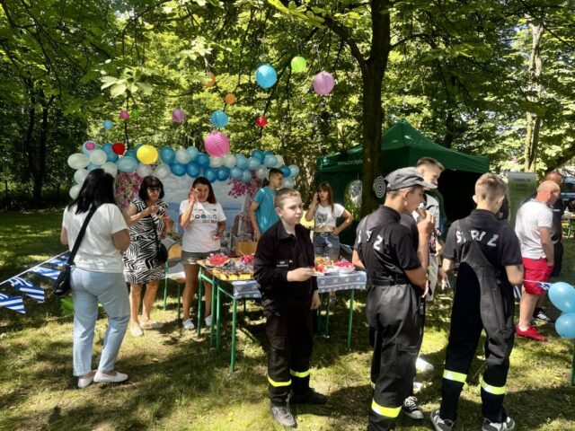 Stoisko event Grecki oraz sąsiadujące z nim stoisko Technikum Leśnego. Uczestnicy i organizatorzy festyn Zawodowe Lato w Bujnach zwiedzają stoiska oraz konsumują przygotowany poczęstunek.