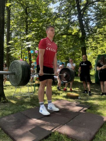Uczeń podnosi ciężary podczas festynu Zawodowe Lato w Bujnach. W tle widzowie tej konkurencji.